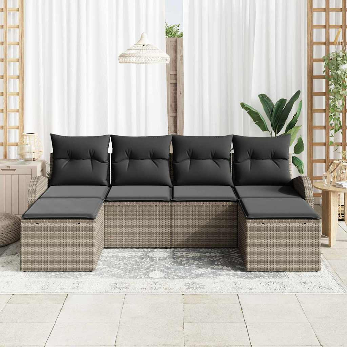 Outdoor-Ecksofa mit grauen Kissen und Rattangestell. Auf einem gemusterten Teppich, mit weißen Vorhängen im Hintergrund.
