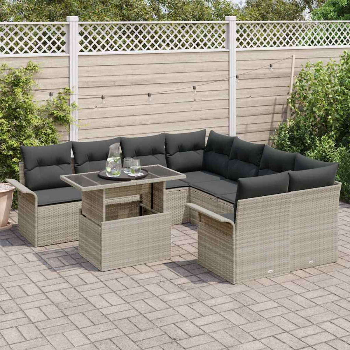 Eine Terrassengarnitur mit grauen Kissen und einem Glastisch. Im Hintergrund ein weißer Zaun und Grün.