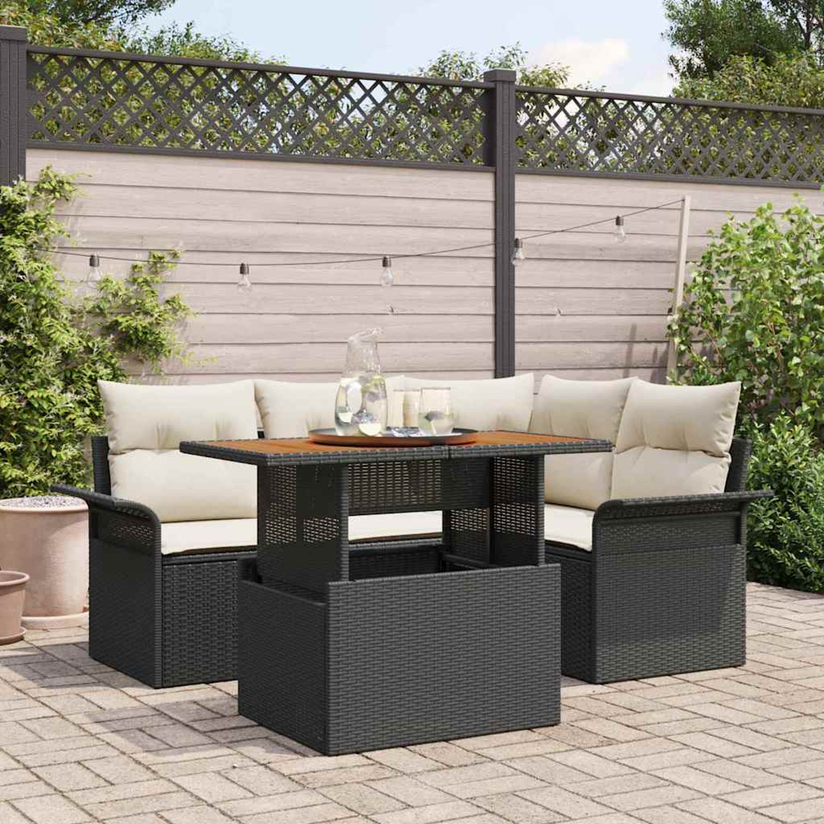Gartenmöbel-Set aus Rattan. Ein Tisch, zwei Sofas mit cremefarbenen Kissen und eine Aufbewahrungsbox. Eine Kanne und Gläser stehen auf dem Tisch.