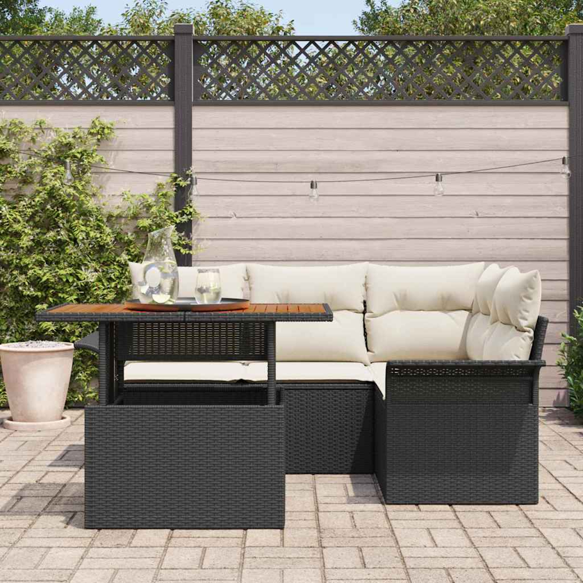Terrassenset mit schwarzer Korbmöbel, hellen Kissen und einem Holztisch. Hintergrund: Zaun und Pflanzen.