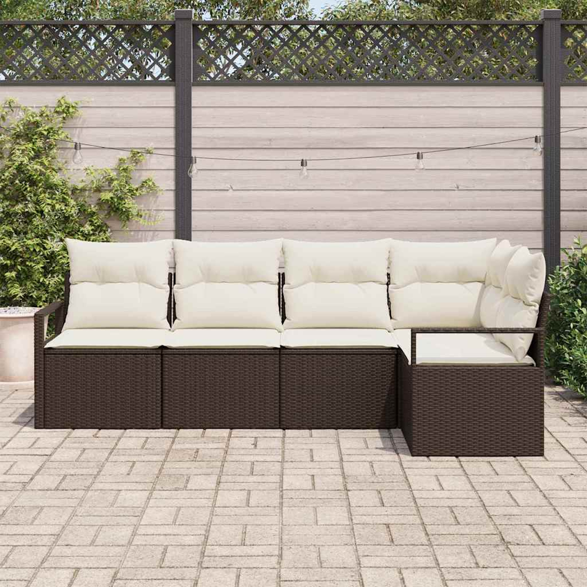 Ein braunes Outdoor-Geflecht-Ecksofa mit cremefarbenen Kissen steht auf einer Ziegelstein-Terrasse. Im Hintergrund befindet sich ein Holzzaun.