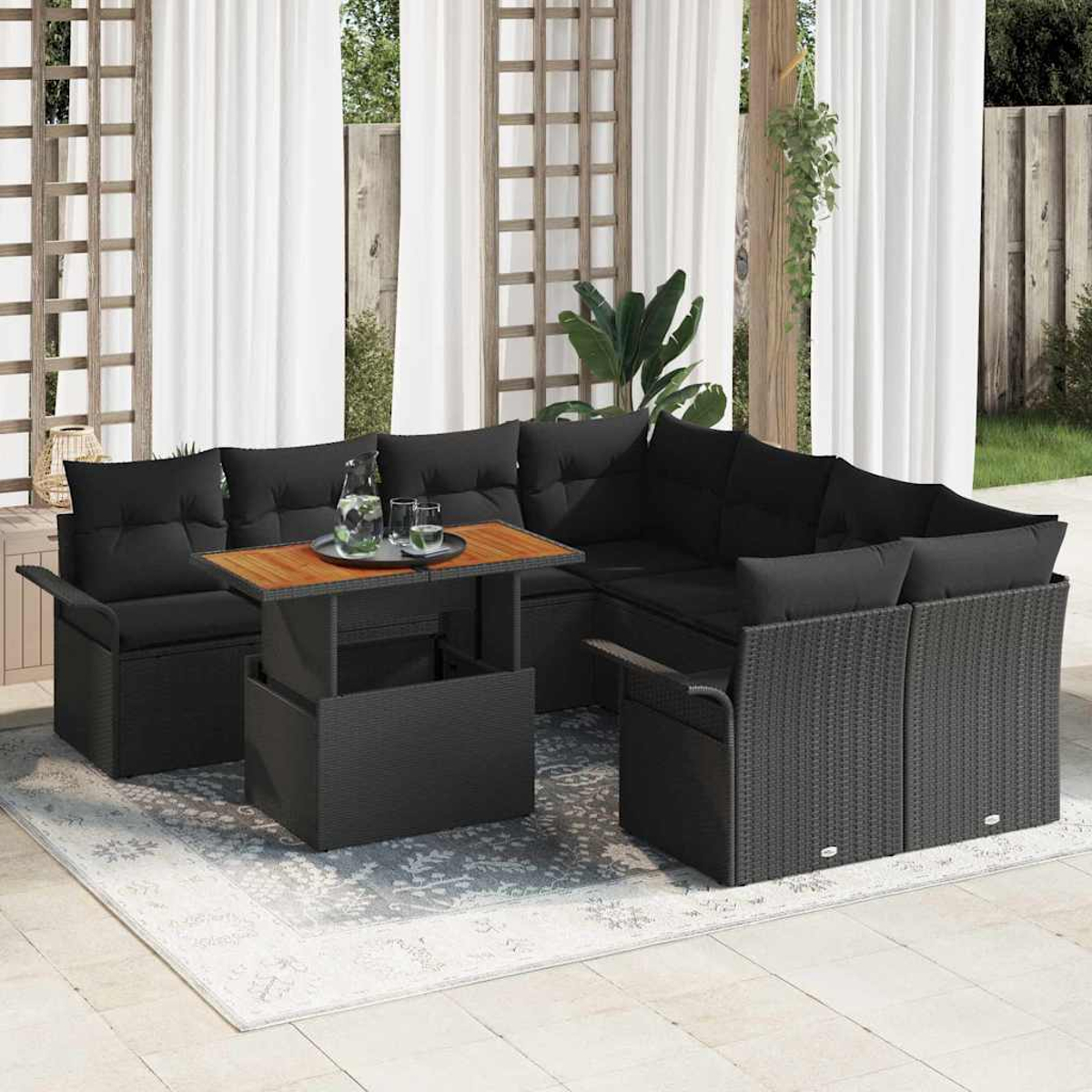 Outdoor-Ecksofa mit schwarzen Kissen, einem Holztisch mit Getränken und einem Teppich. Weiße Vorhänge und grüne Pflanzen im Hintergrund.