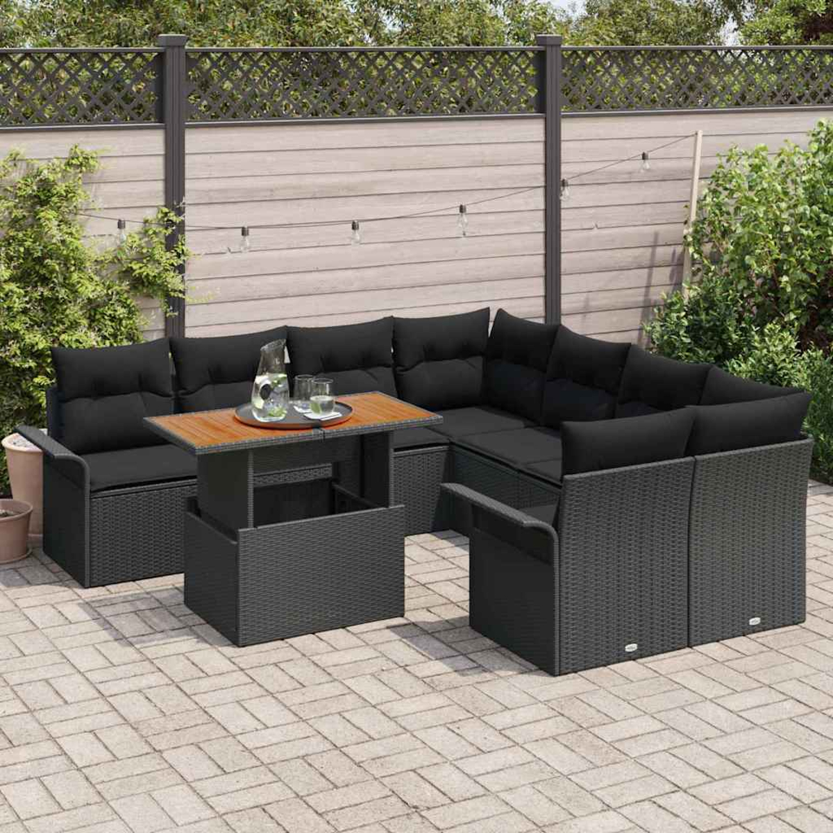 Garten-Sitzgruppe mit schwarzen Kissen und einem Holztisch auf einer Terrasse. Im Hintergrund befinden sich ein Zaun und Grün.