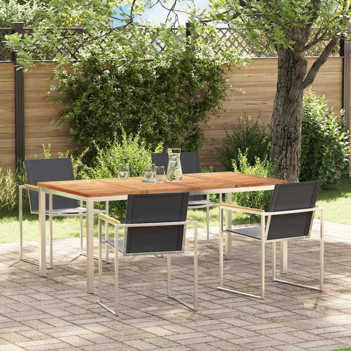 Essgruppe im Freien: Holztisch, Metallstühle, Gläser und eine Kanne mit Früchten. Auf einer Backstein-Terrasse, umgeben von Grün.
