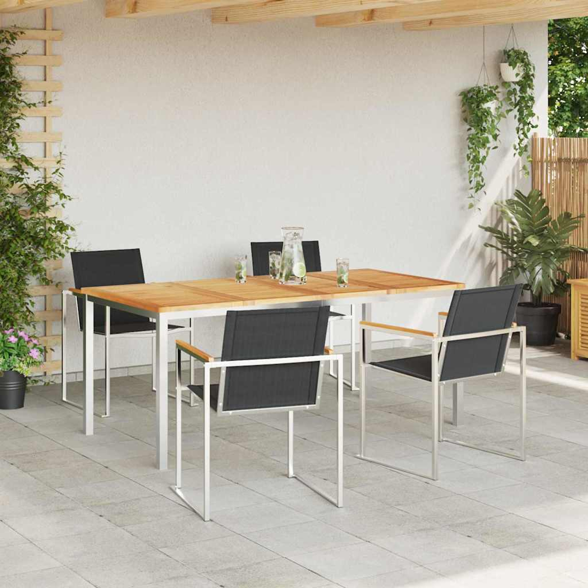 Essgruppe im Freien mit Holztisch, vier schwarzen Stühlen und Getränken. Pflanzen und eine weiße Wand im Hintergrund.