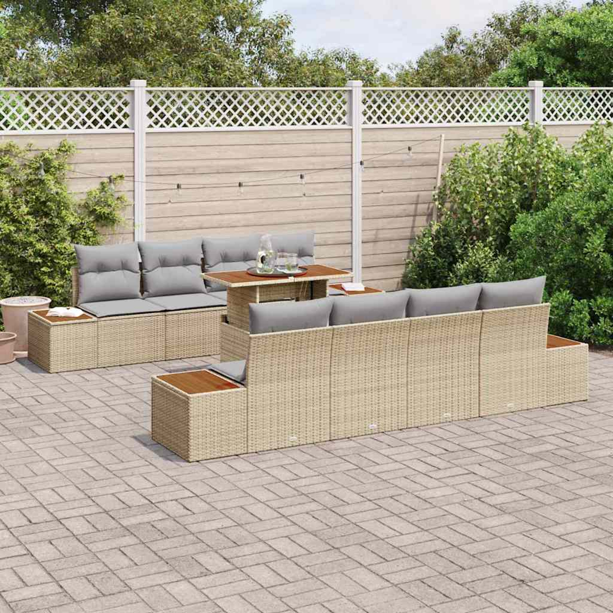 Garten-Sitzgruppe auf einer Terrasse. Beige gewebte Möbel mit grauen Kissen, ein Holztisch und ein weißer Gitterzaun im Hintergrund.