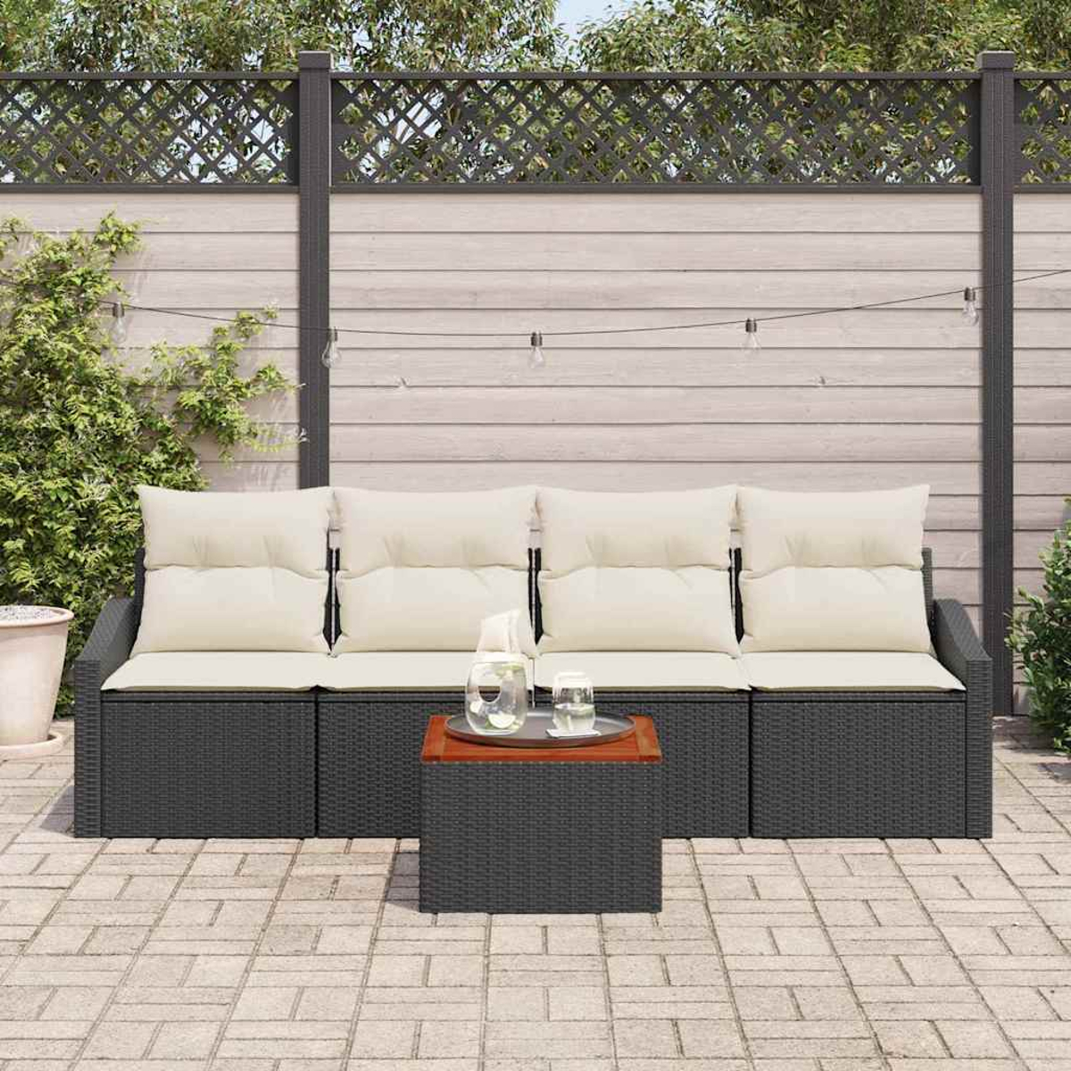Garten-Sitzgruppe auf einer Terrasse. Enthält ein dunkelgraues Korbmöbel-Sofa mit cremefarbenen Kissen, einen kleinen Tisch und einen dekorativen Zaun.