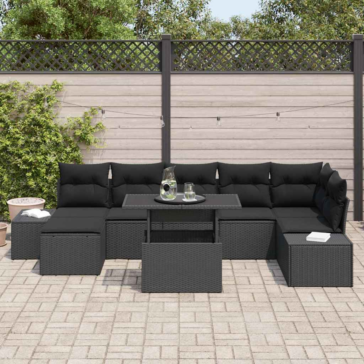 Outdoor-Ecksofa mit schwarzen Kissen und Tisch auf einer Terrasse. Im Hintergrund ein Holzzaun und Grün.