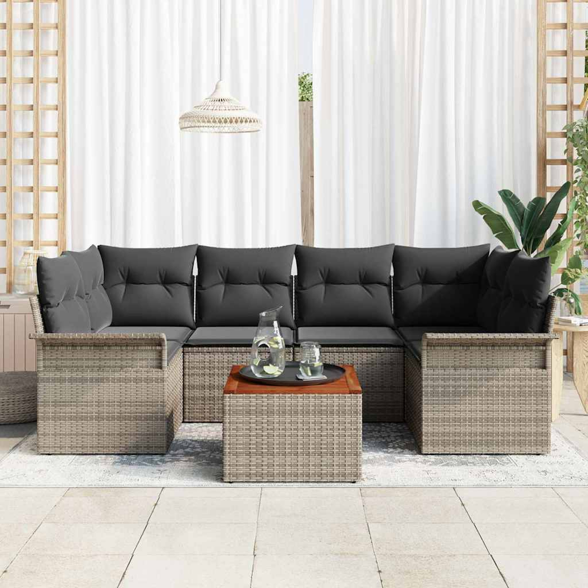 Sofá seccional exterior con cojines grises, una mesa de café de madera y cortinas blancas al fondo.