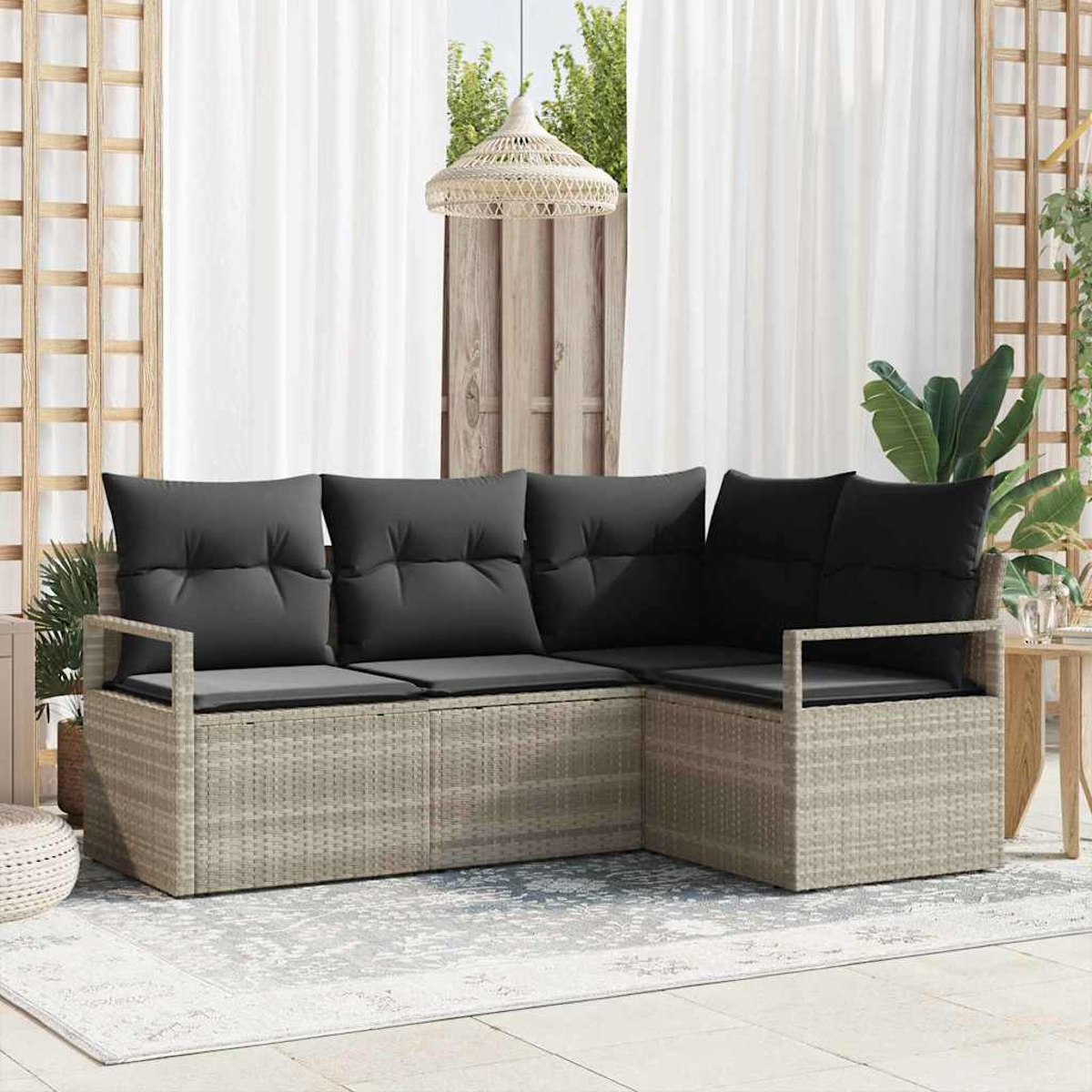 Ein Ecksofa mit schwarzen Kissen steht auf einer Terrasse. Weiße Vorhänge und eine gewebte Leuchte sind im Hintergrund.