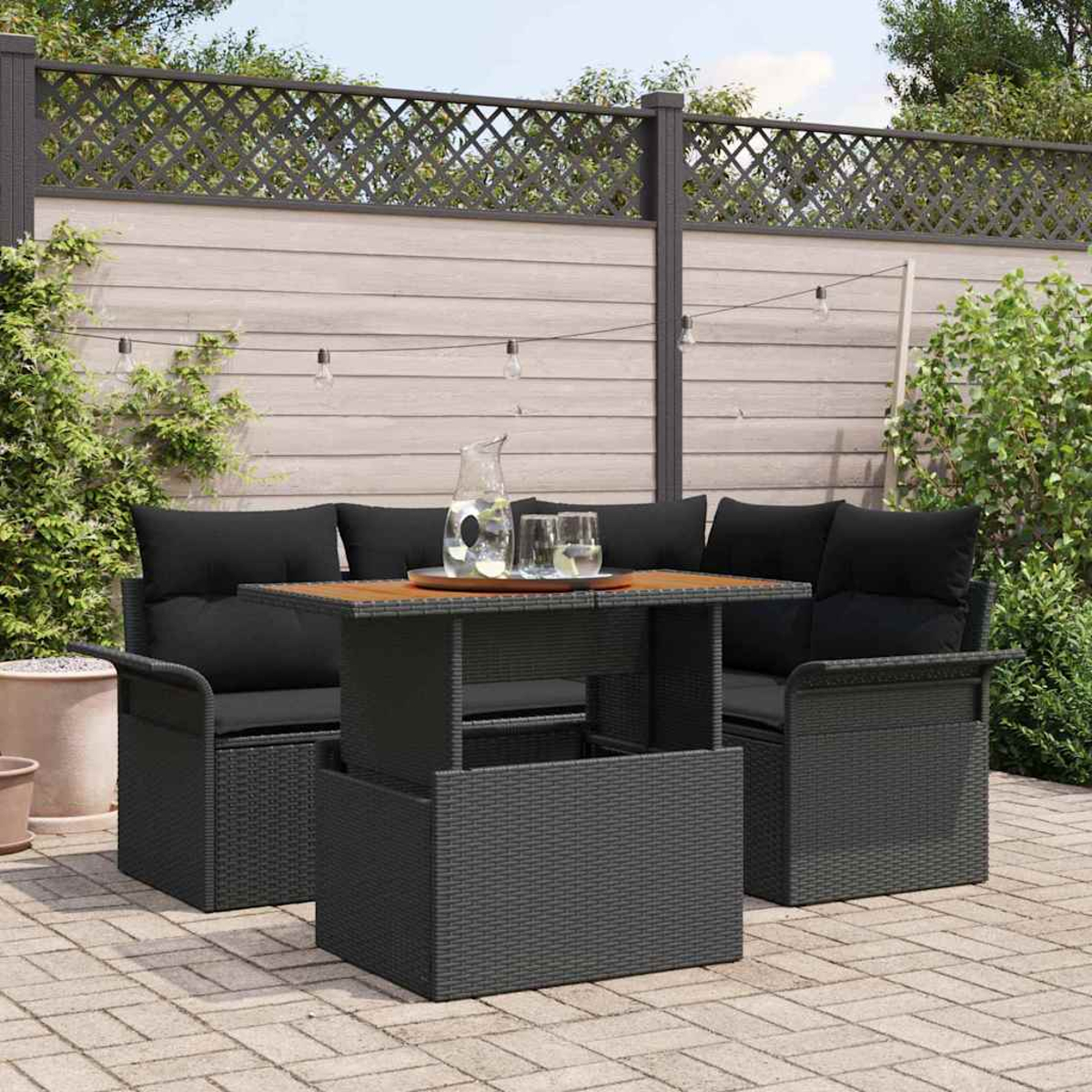 Terrassenset im Freien mit schwarzen Kissen, Holztisch und einem Krug darauf. Das Set befindet sich auf einer Terrasse aus Ziegeln.