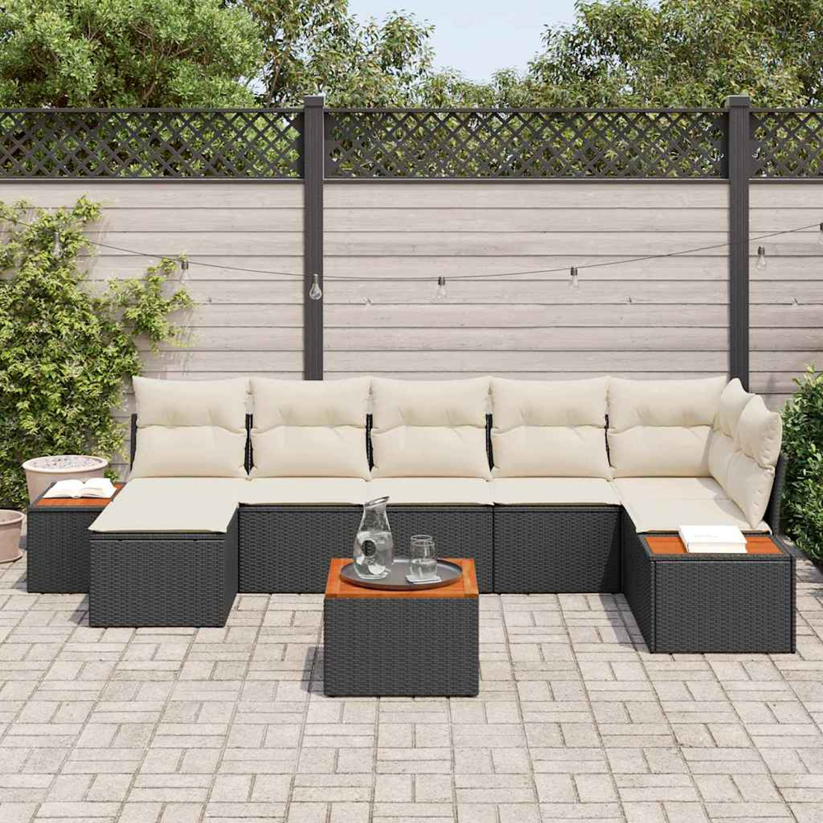 Outdoor-Ecksofa mit cremefarbenen Kissen, zwei Beistelltischen und einem Couchtisch mit Tablett. Vor einem Holzzaun.