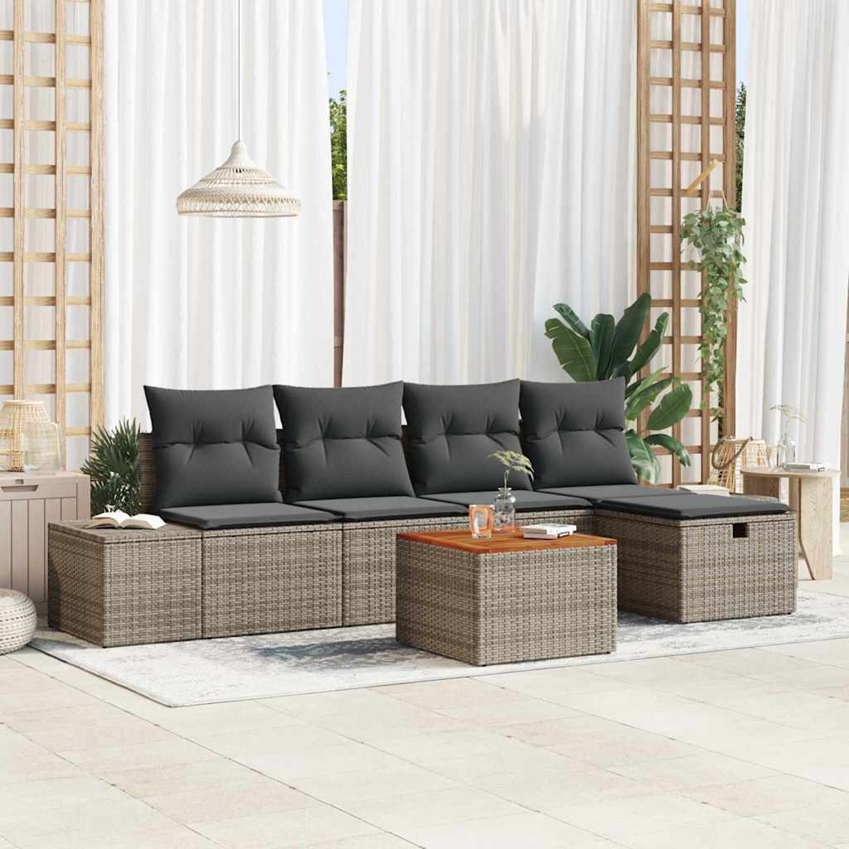 Garten-Sitzgruppe mit grauen Kissen. Davor ein Couchtisch und ein Hocker. Weiße Vorhänge und Pflanzen im Hintergrund.