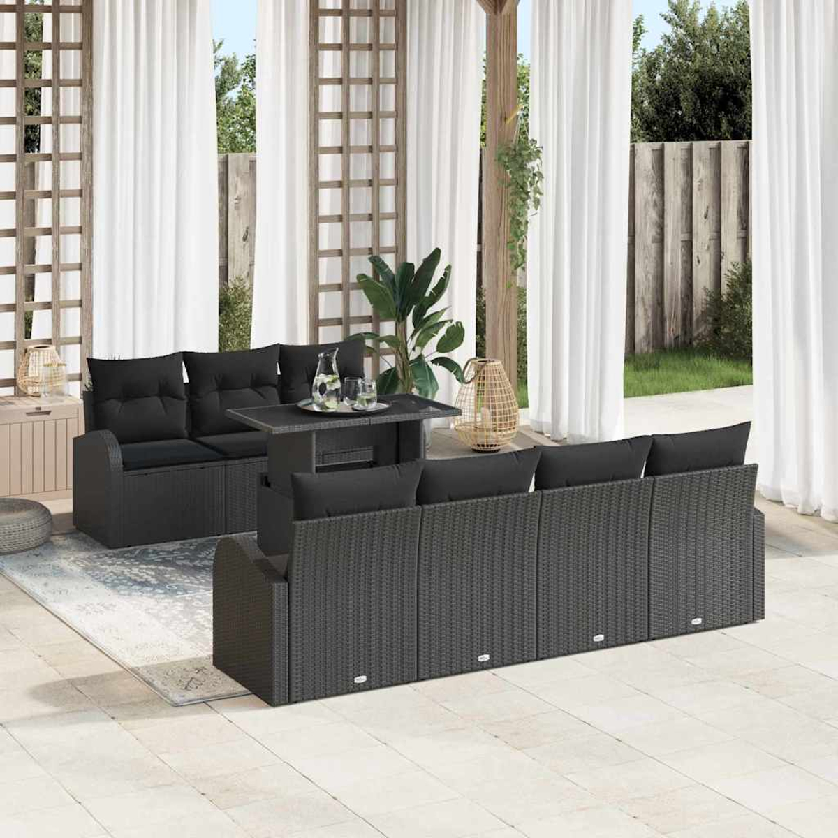 Terrassenset. Dunkelgraues Korbmöbel-Set mit schwarzen Kissen. Weiße Vorhänge, Pflanzen und Holzgitter im Hintergrund.
