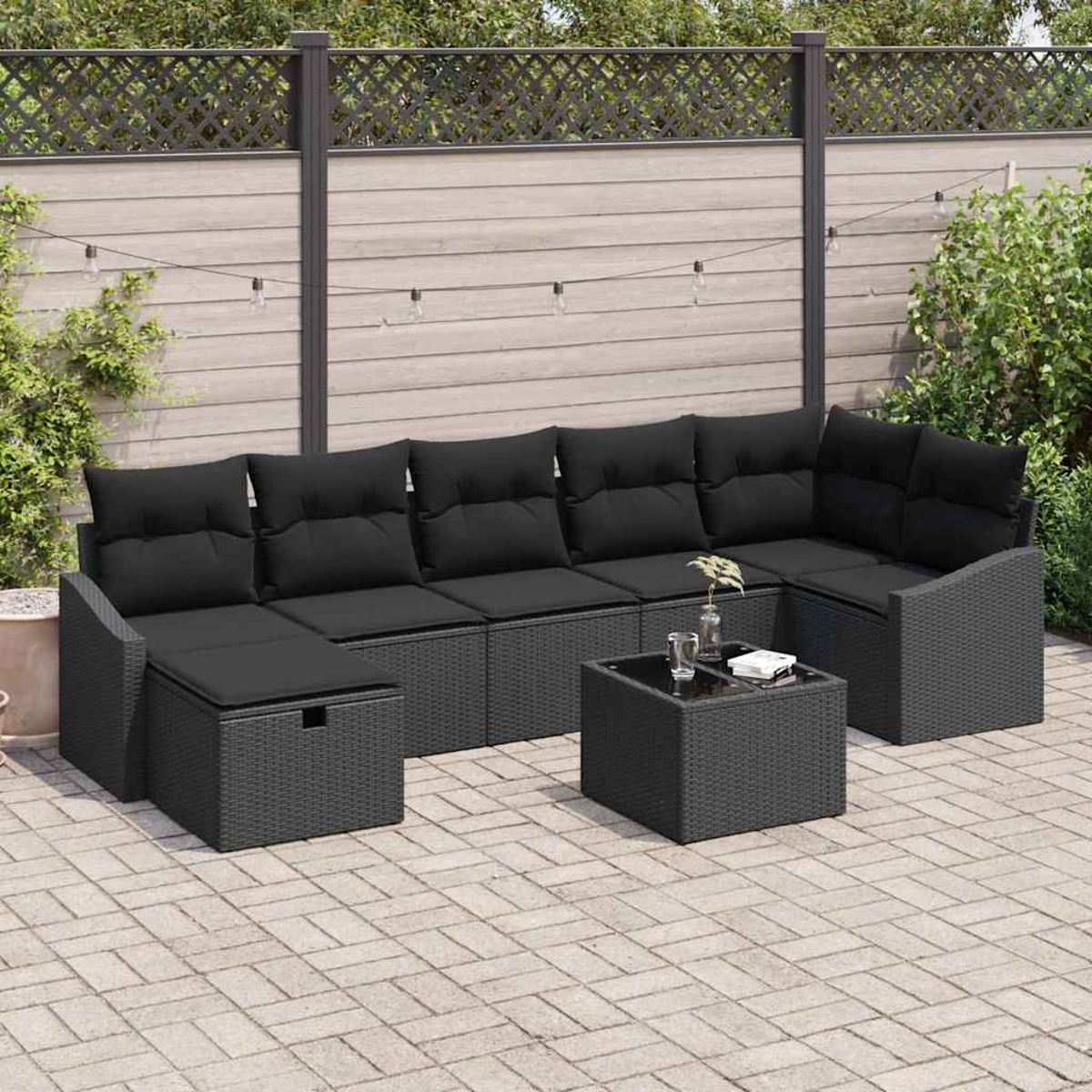 Outdoor-Ecksofa mit schwarzen Kissen und einem kleinen Tisch auf einer Steinterrasse. Im Hintergrund sind ein Zaun und Grün zu sehen.