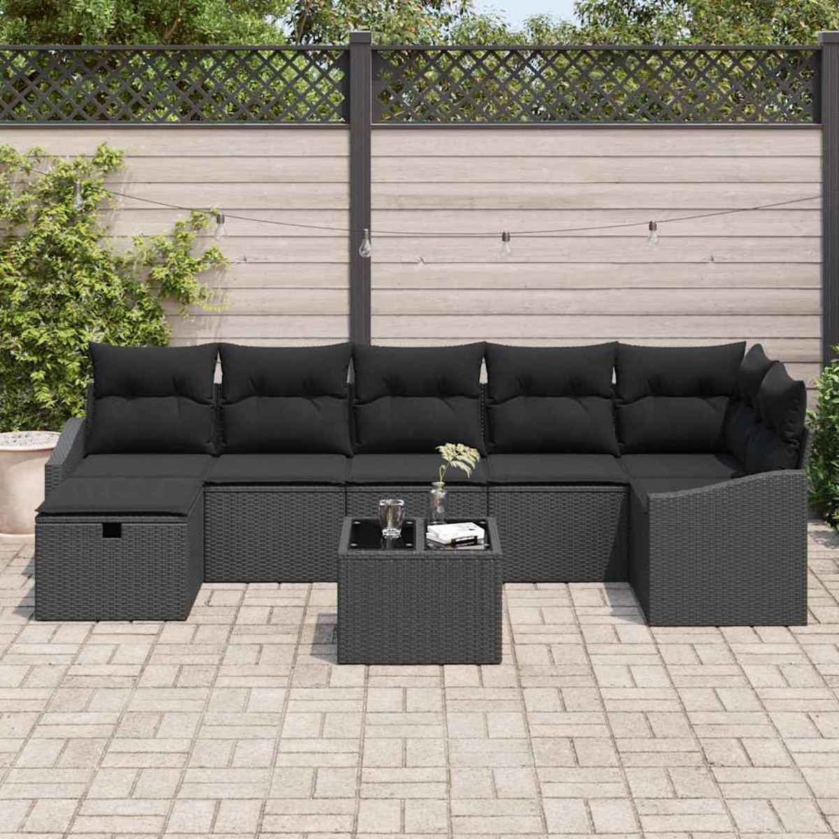 Garten-Sitzgruppe mit schwarzen Kissen auf grauem Korbgeflecht. Davor steht ein kleiner Tisch mit Glas und Buch.
