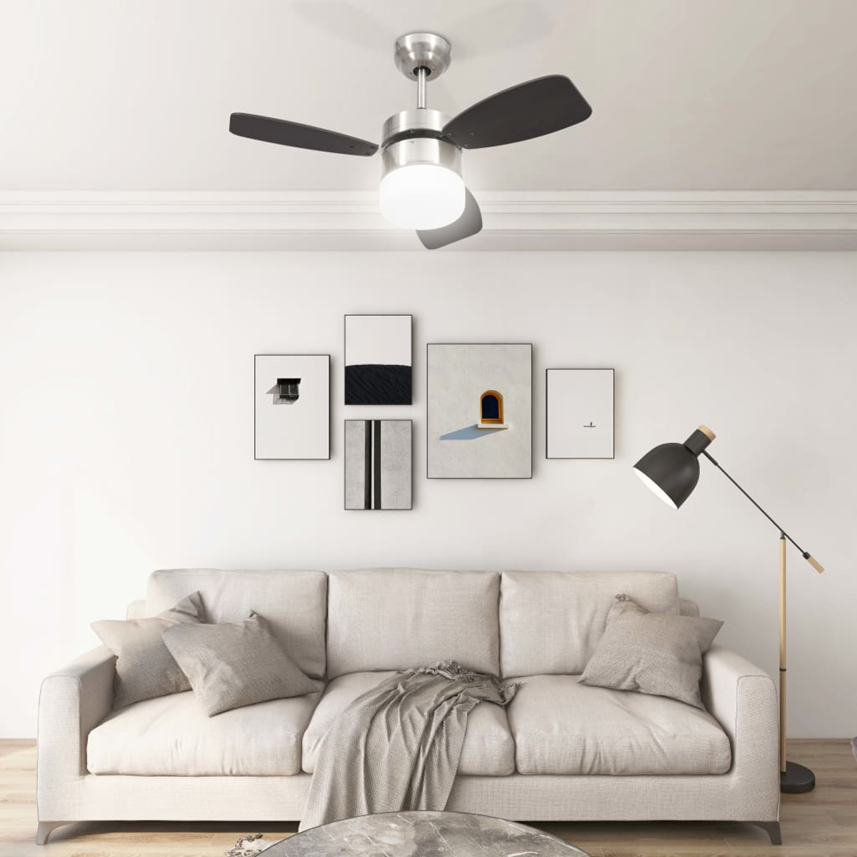 Un soggiorno con ventilatore a soffitto, opere d'arte, un divano con cuscini e una lampada da terra. La stanza ha pareti bianche.