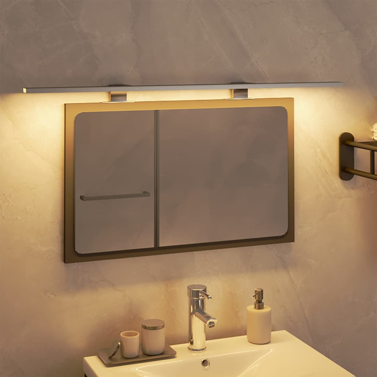 Badezimmerspiegel mit Licht darüber, Waschbecken mit Wasserhahn, Seifenspender und Zubehör auf einer weißen Arbeitsplatte.