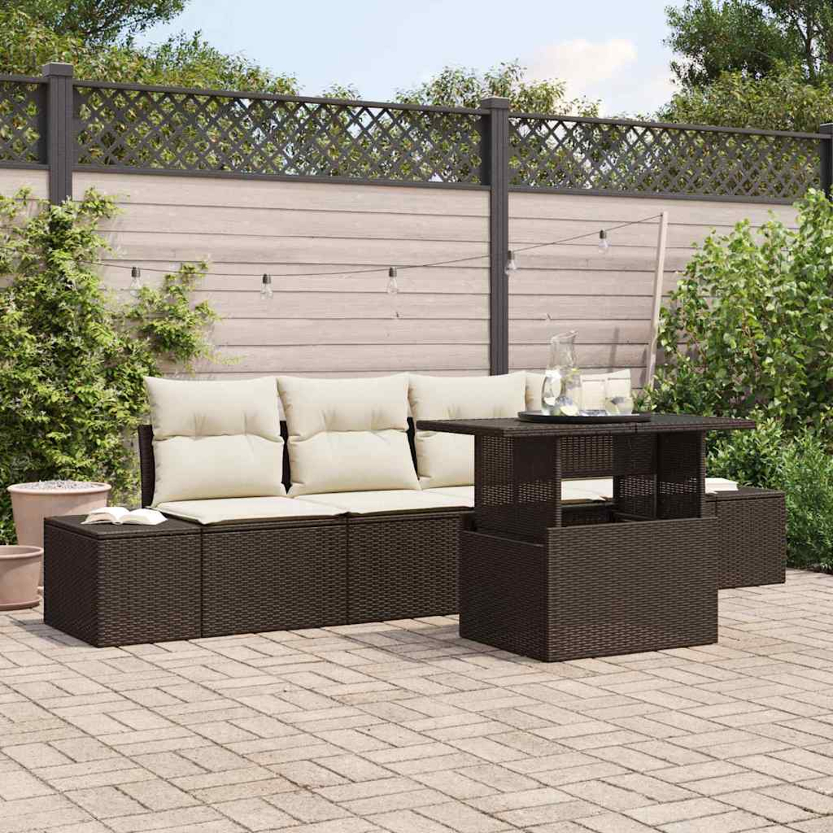 Juego de patio exterior con muebles de mimbre marrón, cojines beige y una mesa elevable en un patio de ladrillos. Fondo con valla.