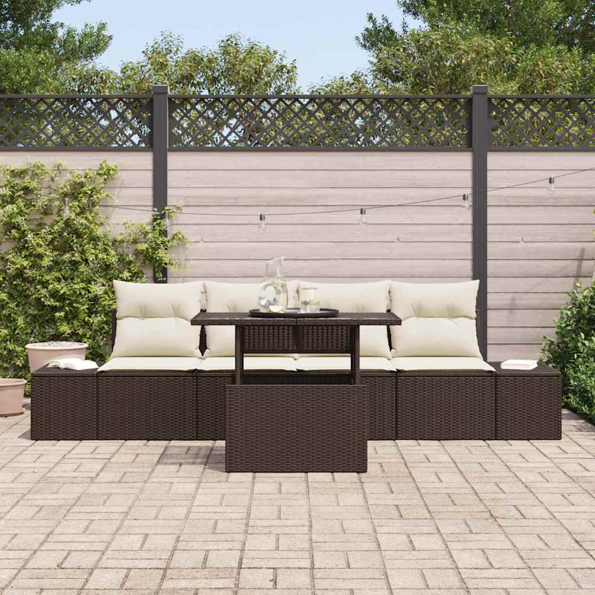 Juego de patio al aire libre con muebles marrones tejidos, cojines crema y una mesa de centro. Respaldado por una valla de madera y vegetación.