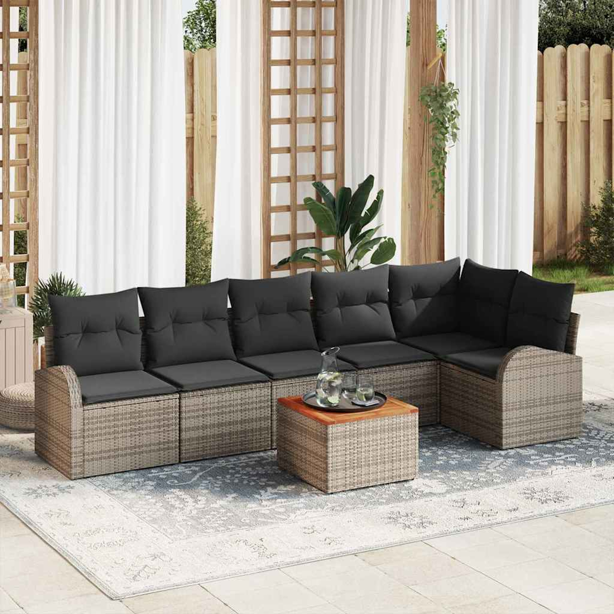 Sofá seccional exterior con cojines grises, una mesa cuadrada y una alfombra. Cortinas blancas y una valla de madera al fondo.