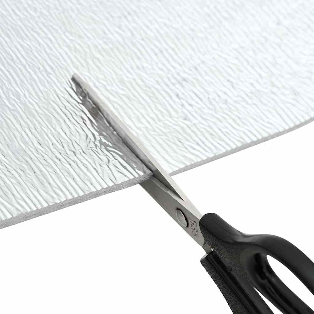 Schere schneidet ein silbernes, strukturiertes Material. Die Schere hat schwarze Griffe. Das Material scheint Isolierung zu sein.