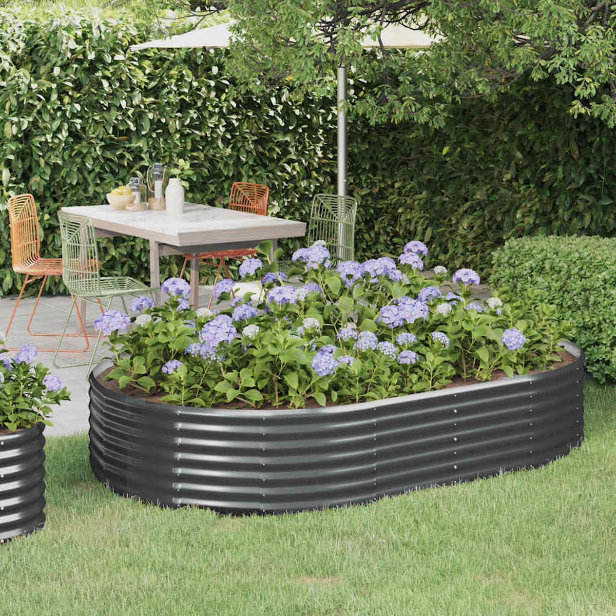 Gartenszene mit einem Metallpflanzgefäß voller blauer Hortensien. Im Hintergrund ein Tisch und Stühle, mit Hecke und Sonnenschirm.