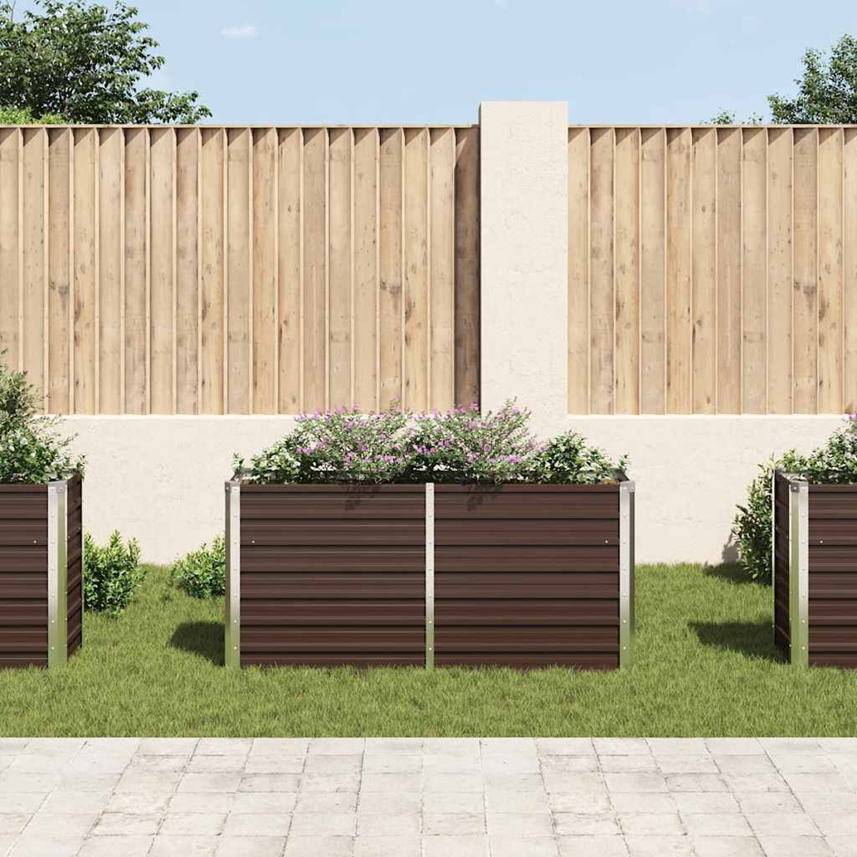 Drei braune Pflanzgefäße mit Blumen stehen auf Gras. Dahinter ein Holzzaun und eine weiße Wand. Gepflasterter Boden davor.