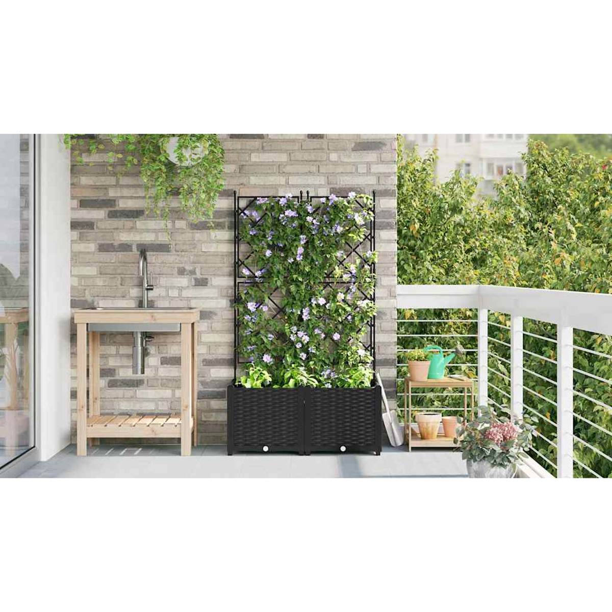 Balcone con muro di mattoni, lavandino in legno e traliccio nero con piante. Vasi, pala e fiori su uno scaffale. Ringhiera bianca.