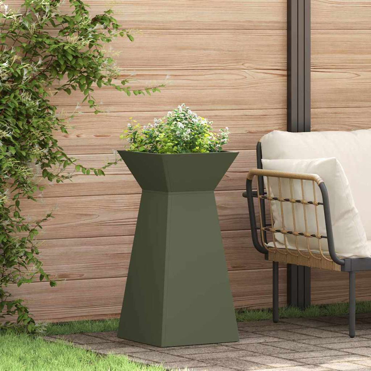 Una fioriera verde oliva con fiori è su un patio. Una sedia con cuscini è a destra. Una recinzione di legno è sullo sfondo.