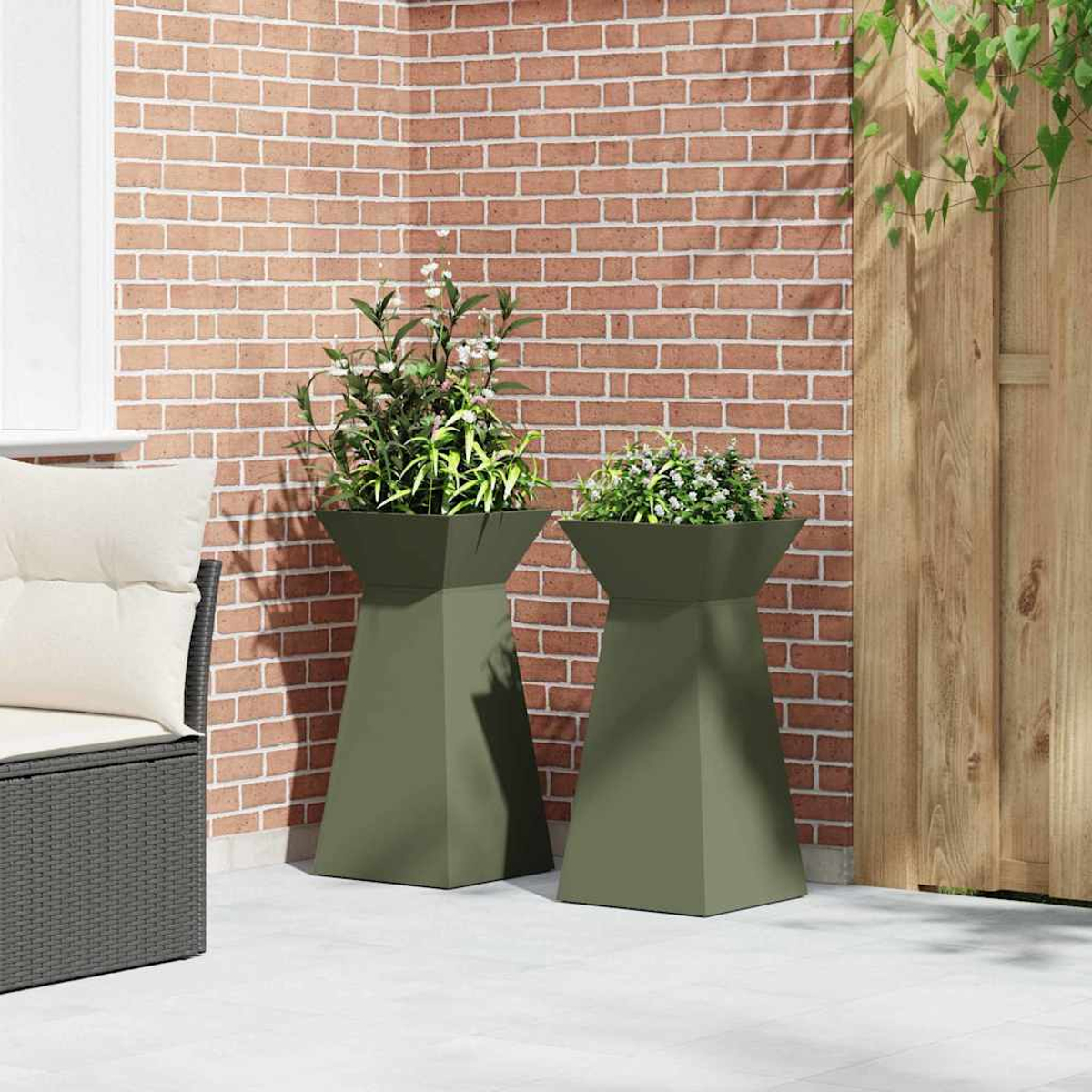 Due fioriere verde oliva con piante su un patio. Un muro di mattoni e una recinzione in legno sullo sfondo.