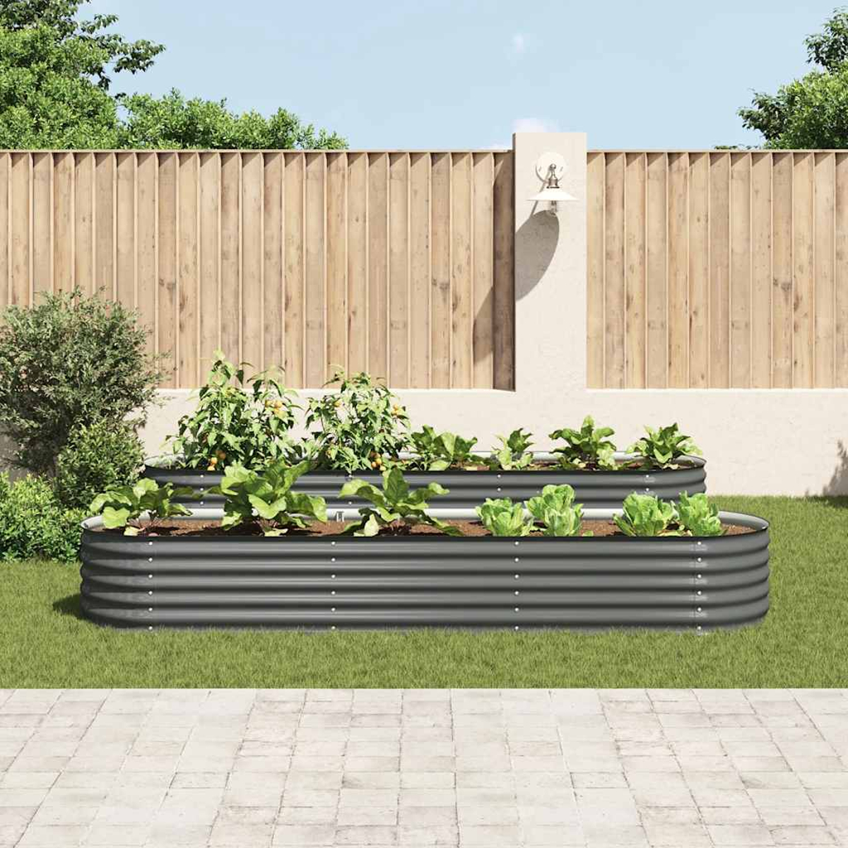 Zwei erhöhte Gartenbeete mit Gemüse stehen auf Gras. Ein Holzzaun und eine Beton-Terrasse sind im Hintergrund.