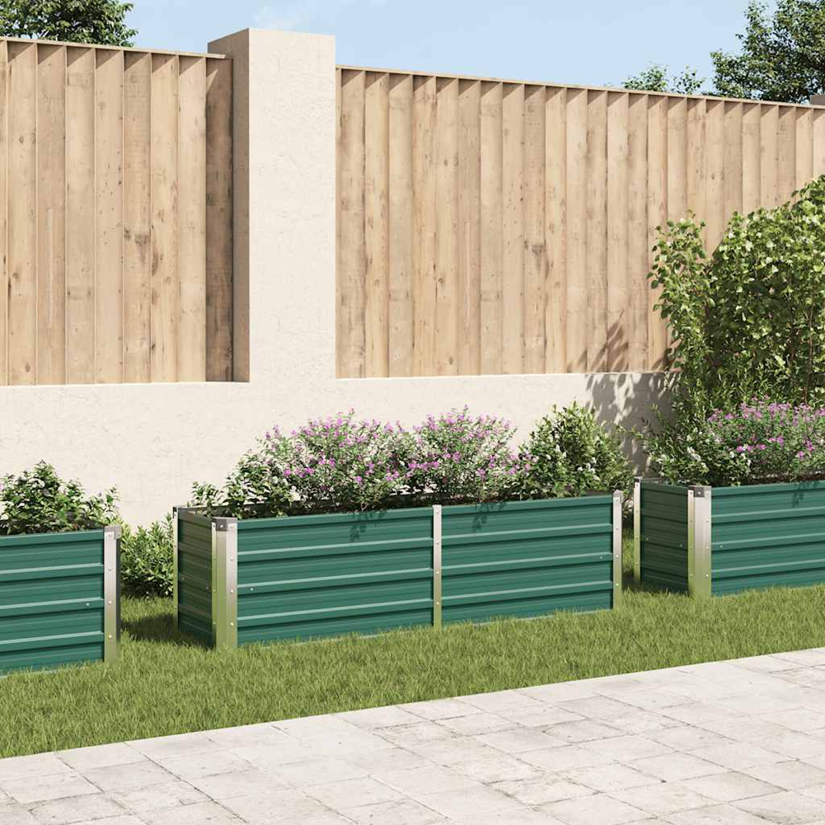 Drei grüne Metallpflanzkästen mit lila Blumen auf Gras. Dahinter ein Holzzaun und eine helle Wand.