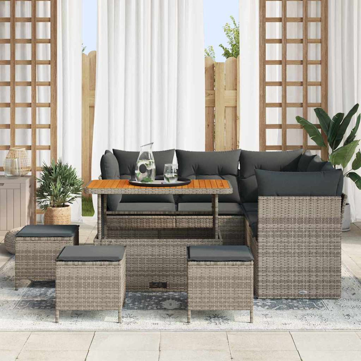 Gartenmöbel-Set mit grauem Sofa, Tisch und Hockern. Pflanzen und Vorhänge im Hintergrund. Die Szene spielt sich im Freien ab.