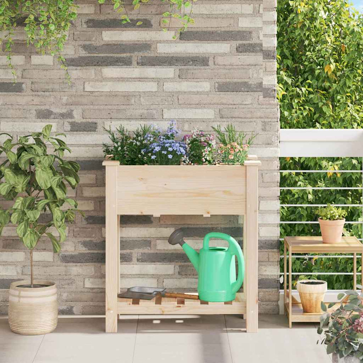 Una fioriera di legno con fiori, un annaffiatoio verde e un tavolino con un vaso a destra. Un muro di mattoni sullo sfondo.