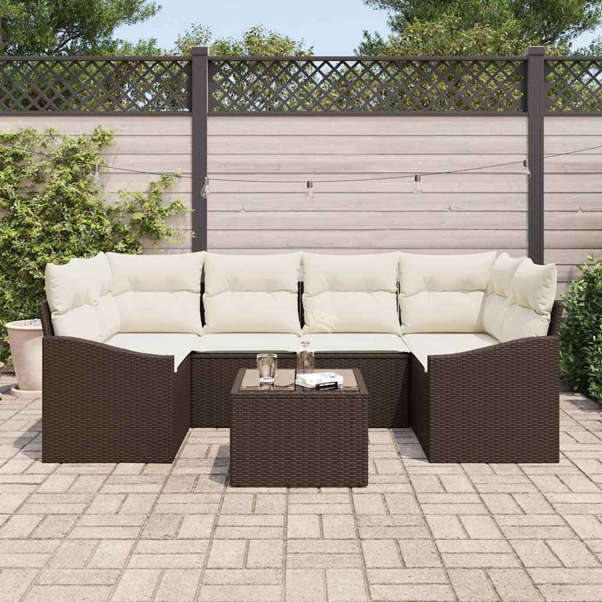Gartenmöbel-Set: braunes Korbmöbel, weiße Kissen, kleiner Tisch mit Glasplatte und graue Ziegel-Terrasse.