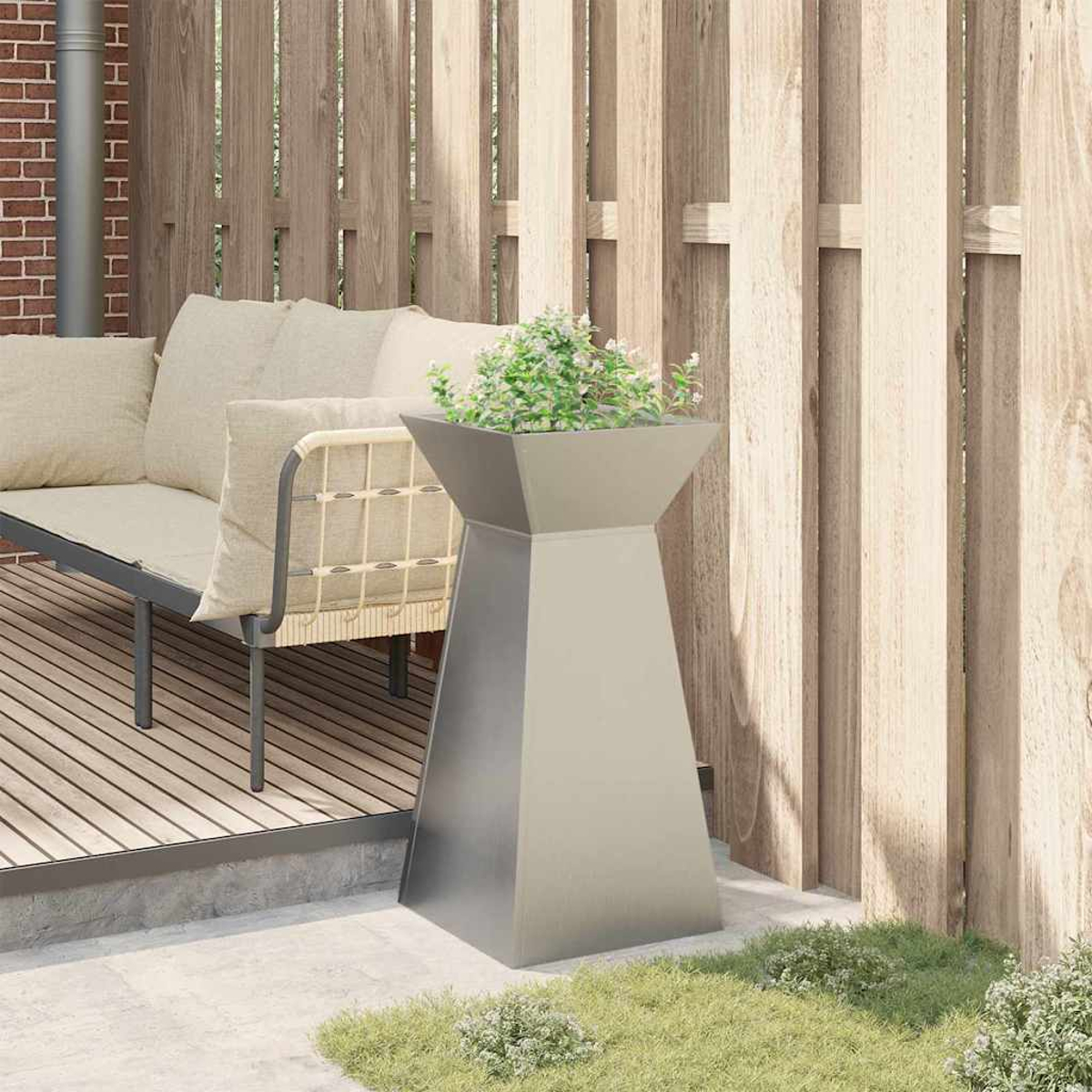 Eine moderne Terrassenszene mit einem Metallpflanzgefäß mit Grün, einem Holzzaun und einem Sofa mit beigen Kissen.