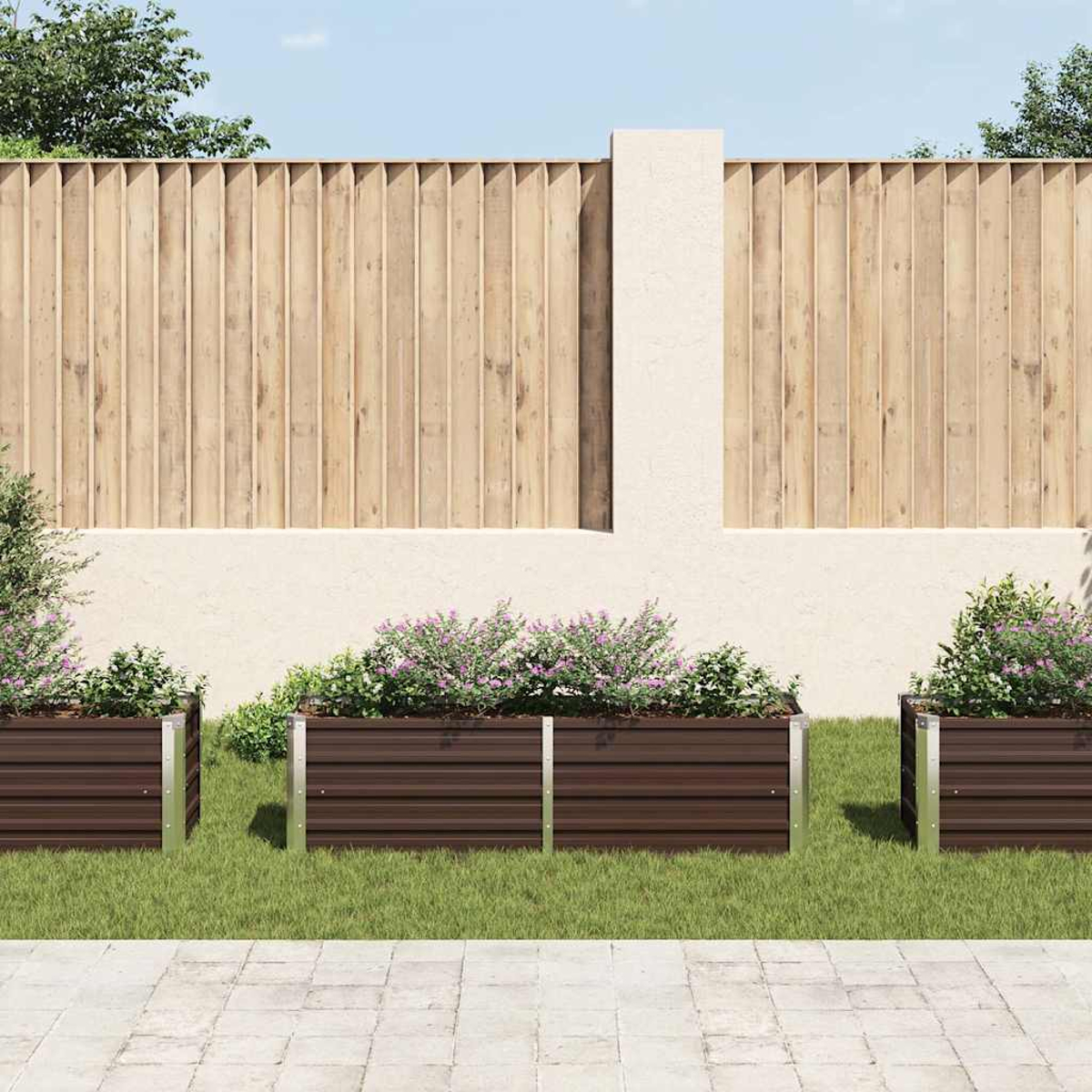 Drei braune Pflanzkästen mit Blumen auf grünem Gras, dahinter ein Holzzaun und eine weiße Wand. Gepflasterter Gehweg davor.