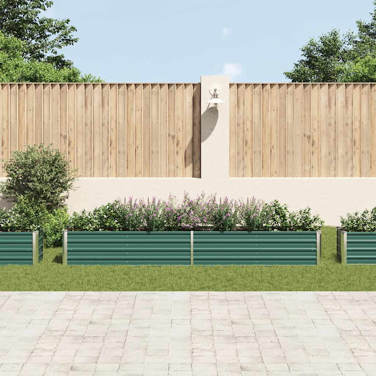 Eine Gartenszene mit grünen Metallpflanzgefäßen, einem Holzzaun und verschiedenen Pflanzen. Im Hintergrund eine weiße Wand und blauer Himmel.