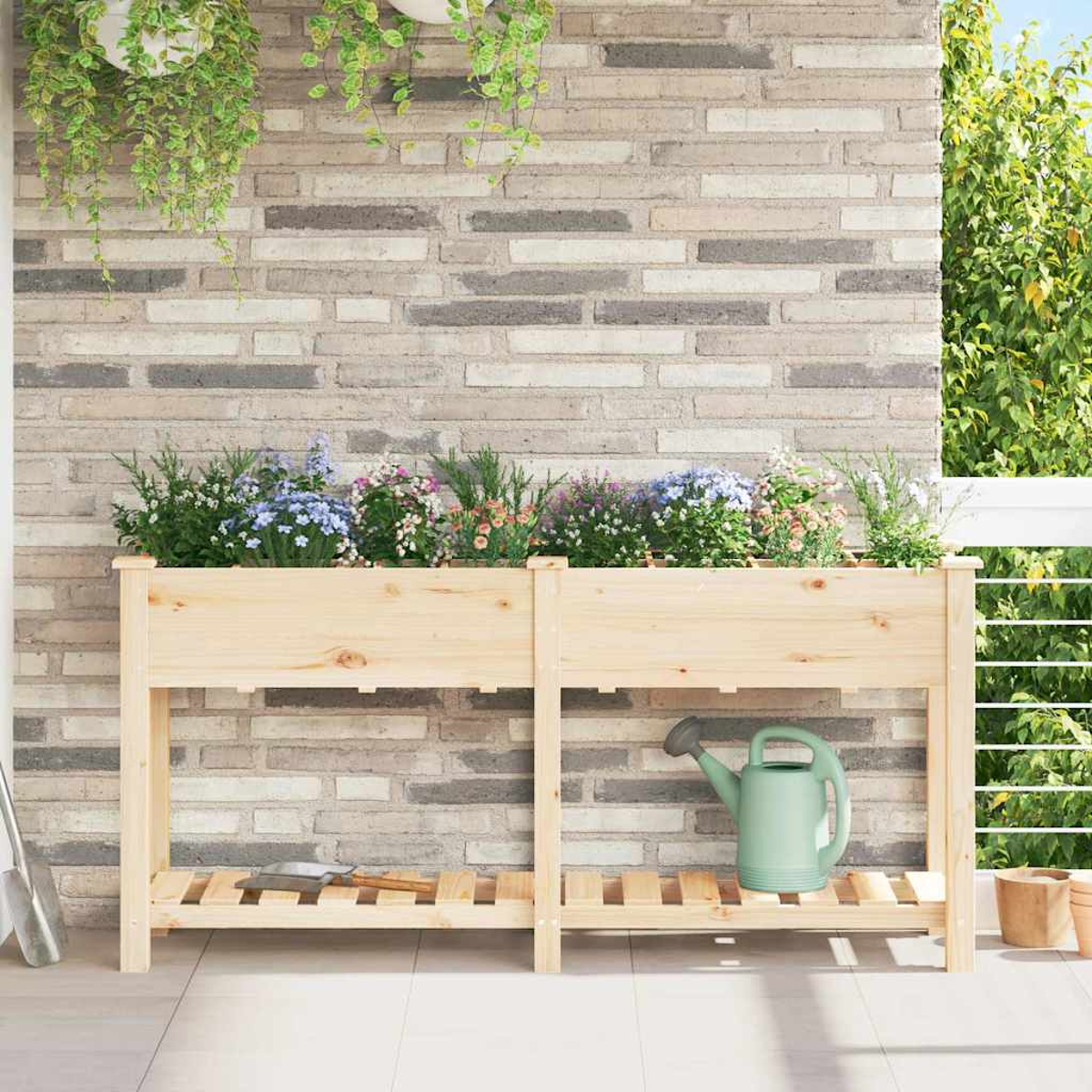 Holzpflanzkasten mit Blumen auf einem Balkon. Eine Gießkanne und eine Schaufel sind vorhanden. Ziegelwand im Hintergrund. Hängepflanzen oben.