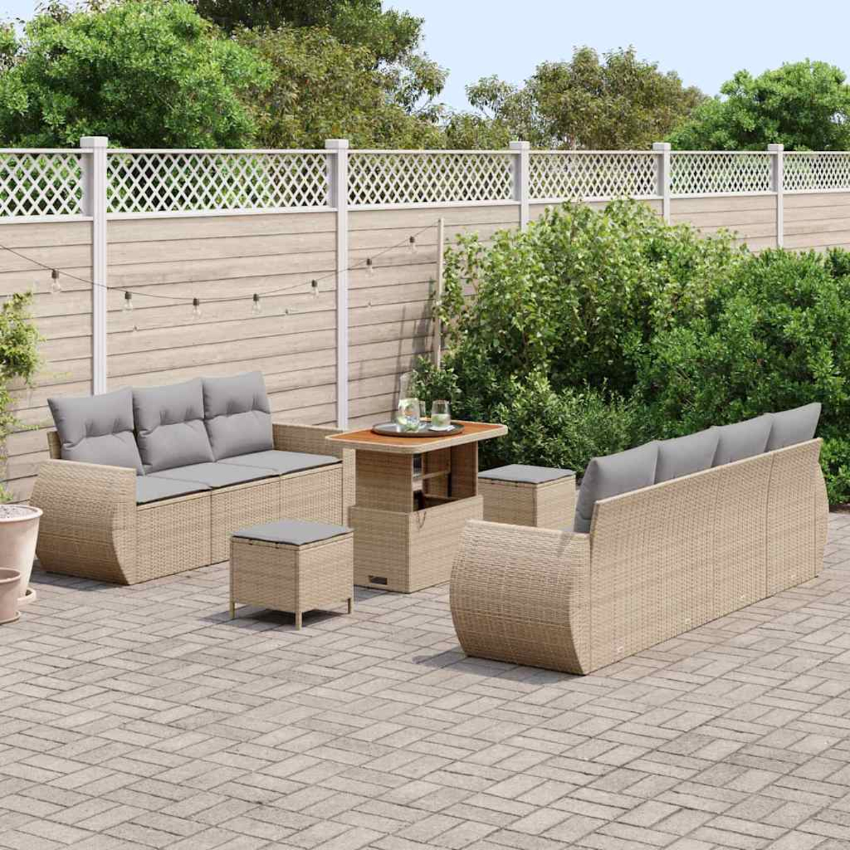 Gartenmöbel-Set. Beige Korbsessel, Tisch und Hocker. Graue Kissen. Backstein-Patio, Holzzaun und grüne Büsche.