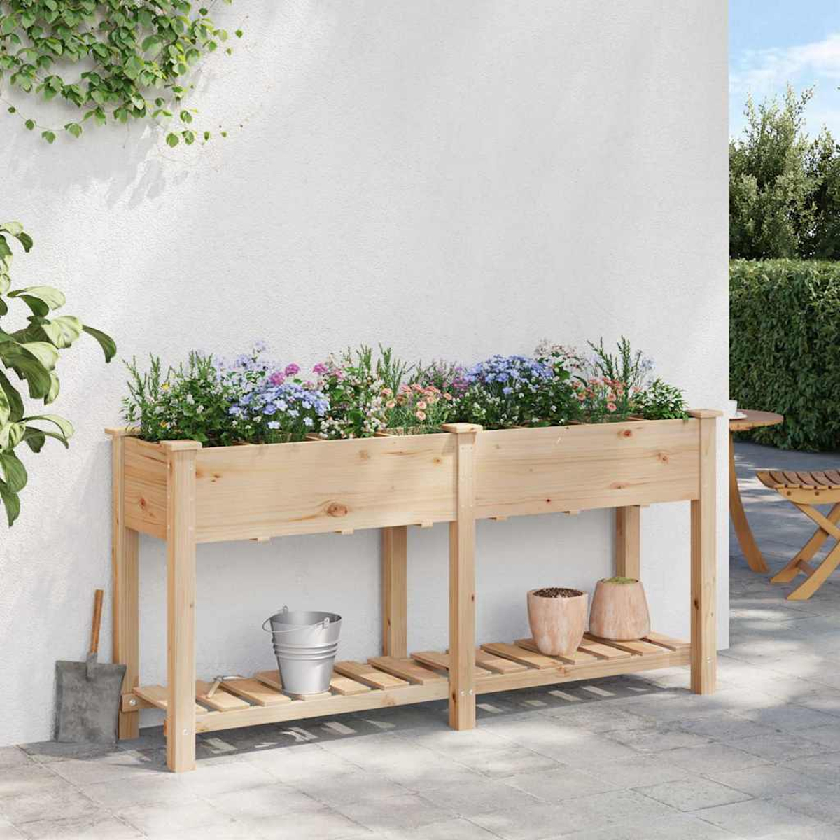 Erhöhte Gartenbeete aus Holz mit Blumen, Töpfen und einer Schaufel. Im Hintergrund eine Wand und grüne Pflanzen.