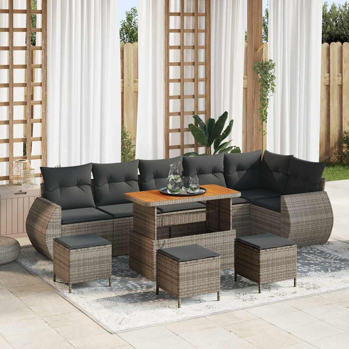 Garten-Terrassenset: graues Korbmöbelsofa, Couchtisch und Hocker. Weiße Vorhänge und Holzzaun im Hintergrund.