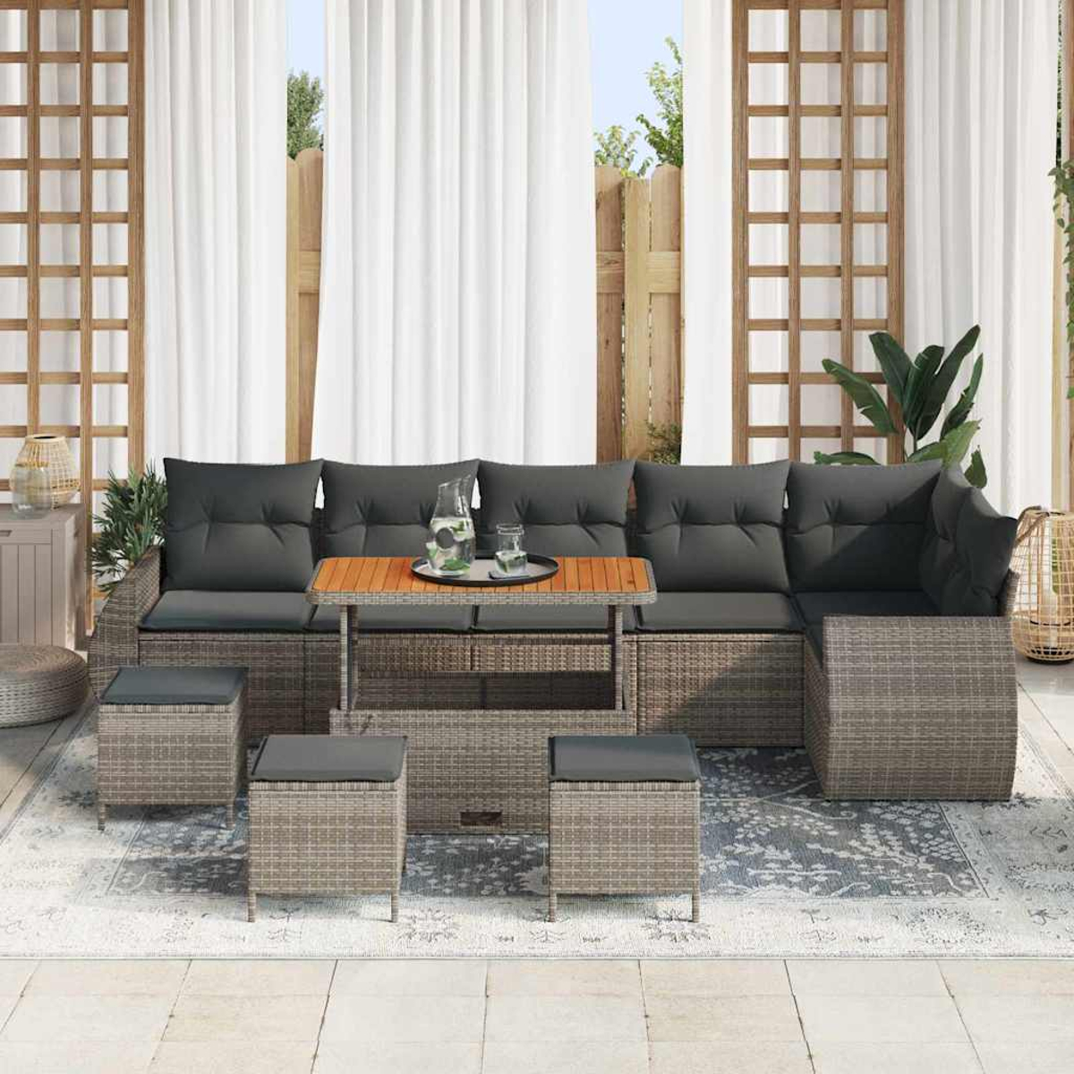 Garten-Set mit grauen Kissen, Holztisch und vier Ottomanen. Weiße Vorhänge und ein Holzzaun im Hintergrund.