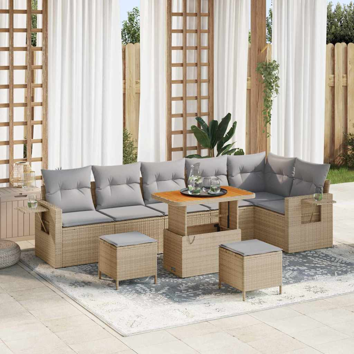 Outdoor-Rattansofa mit grauen Kissen, Hubtisch und zwei Hockern. Auf einem gemusterten Teppich mit transparentem Vorhanghintergrund.