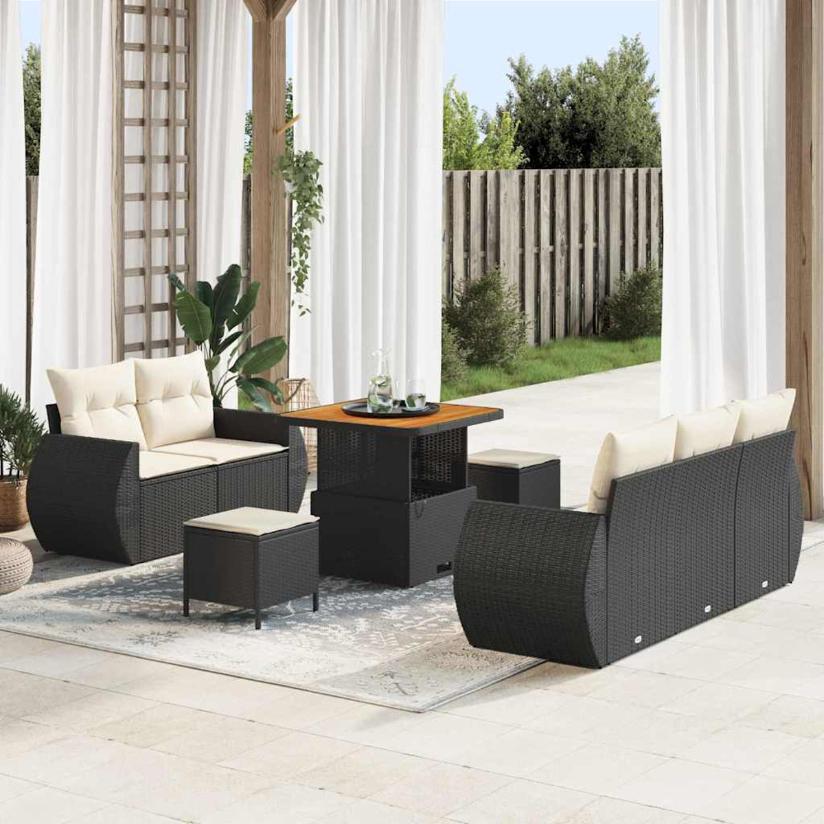 Terrassenmöbel-Set mit schwarzen Korbmöbeln und cremefarbenen Kissen. Beinhaltet einen Tisch, ein Sofa und zwei Ottomanen, auf einem Teppich.
