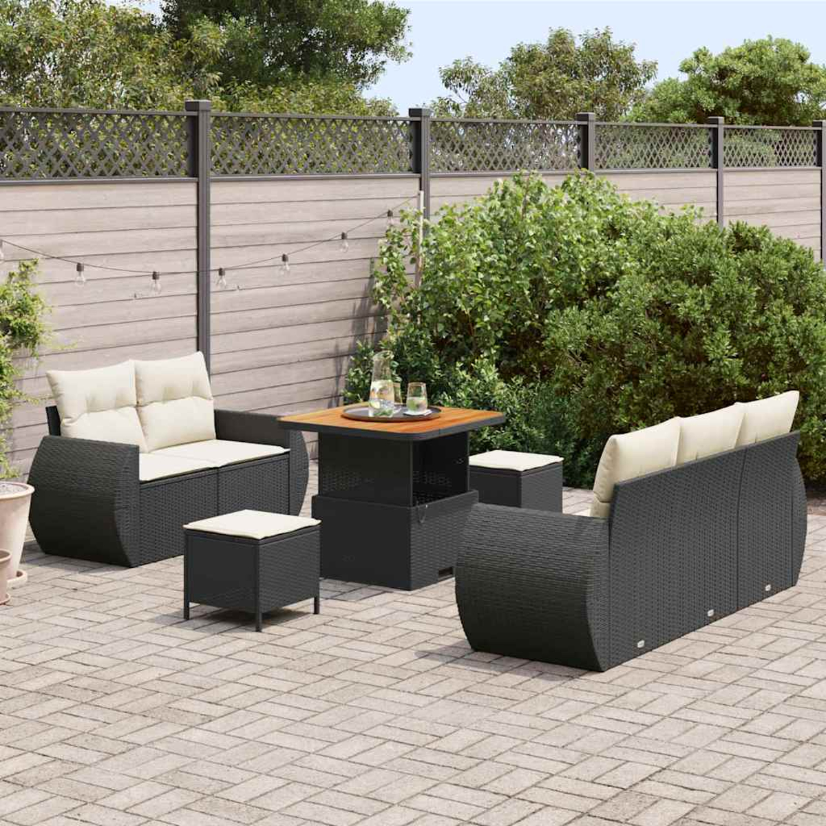 Garten-Terrassenset mit schwarzen Korbmöbeln, beigen Kissen, einem Tisch und zwei Hockern auf einer Ziegelterrasse, mit Holzzaun im Hintergrund.