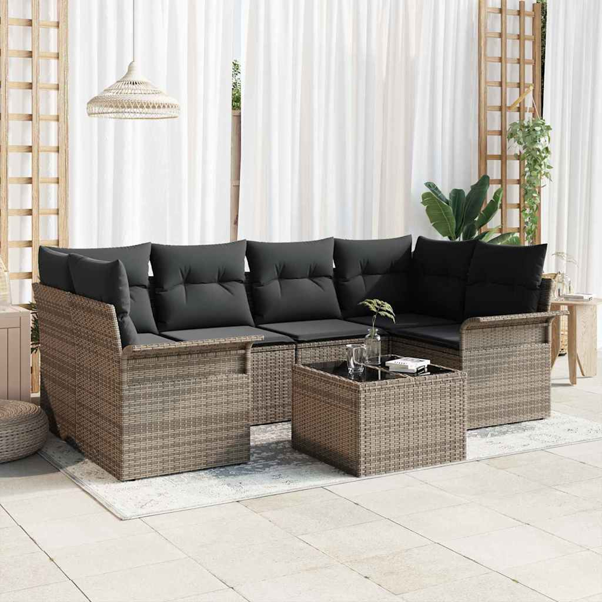 Outdoor-Rattan-Ecksofa mit schwarzen Kissen, einem Couchtisch und weißen Vorhängen im Hintergrund. Eine Hängepflanze ist sichtbar.