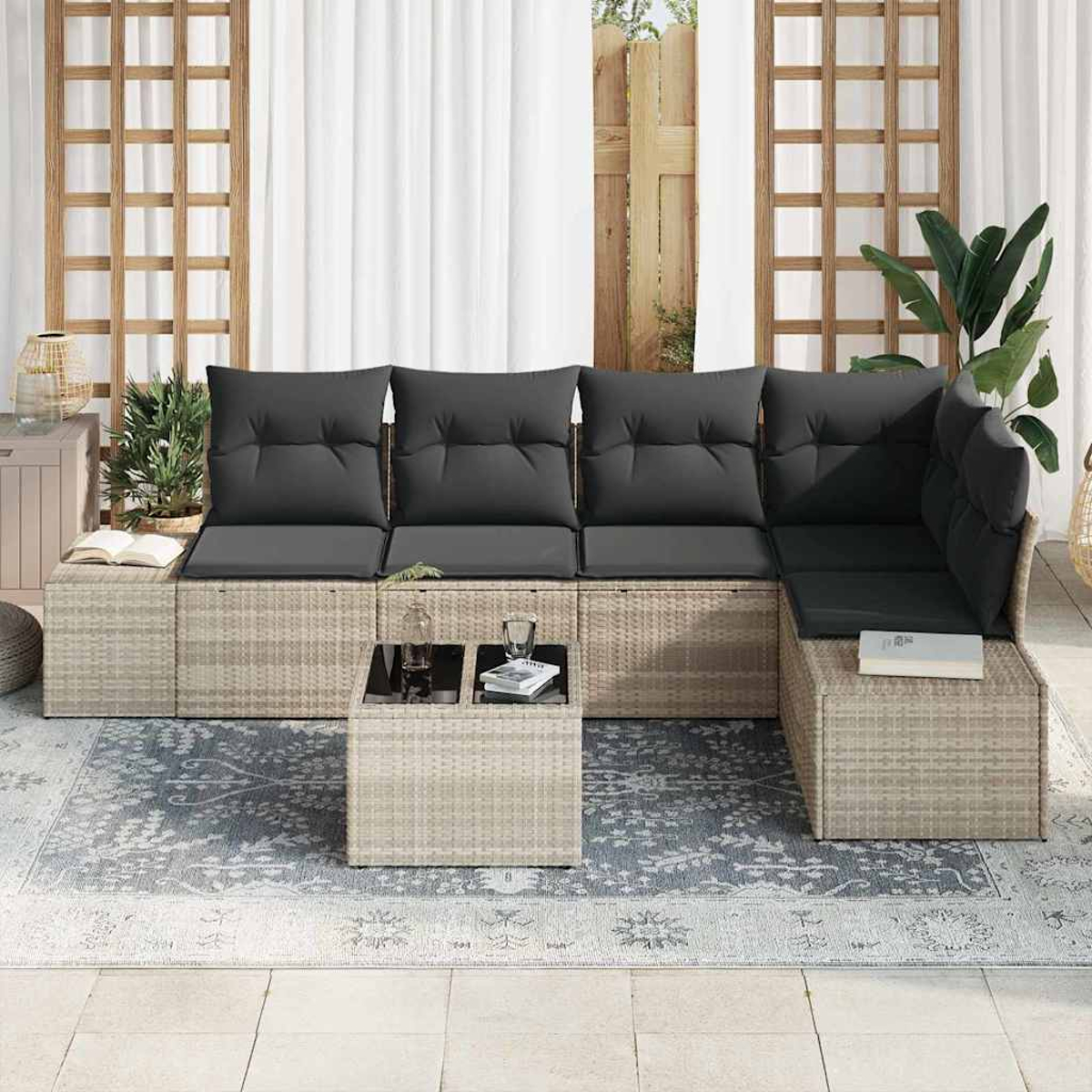 Outdoor-Ecksofa mit grauen Kissen. Davor steht ein kleiner Tisch mit Büchern und Gläsern. Auf dem Boden liegt ein gemusterter Teppich.