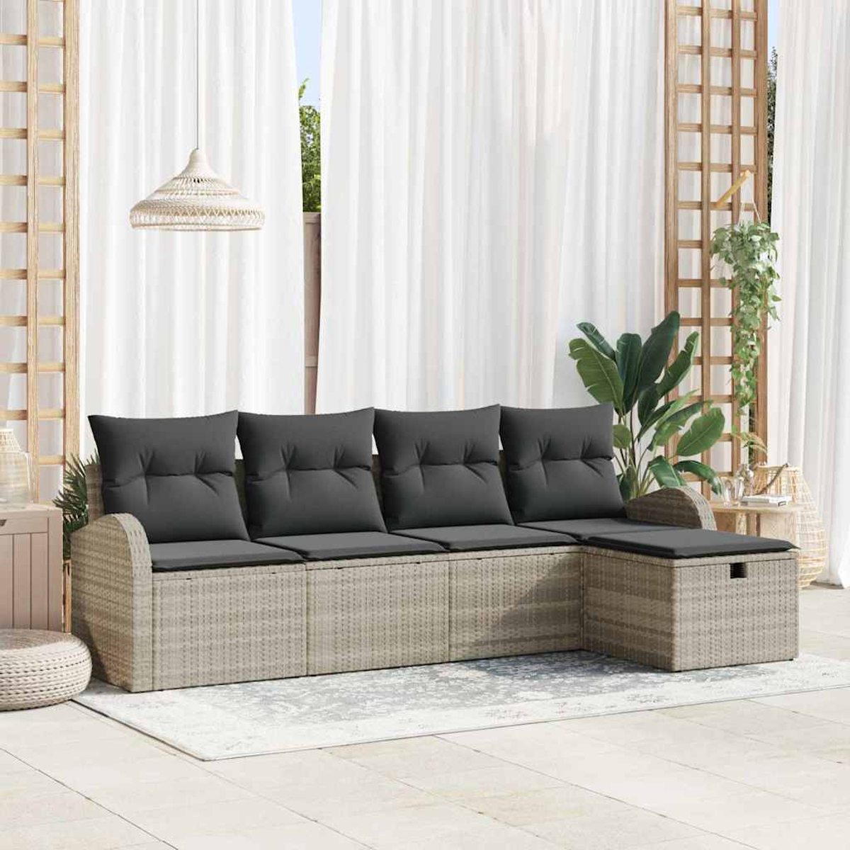 Ein graues, gepolstertes Outdoor-Sofa steht auf einer Terrasse. Dahinter befinden sich weiße Vorhänge, Holzgitter und Hängepflanzen. Ein gewebter Lampenschirm hängt.